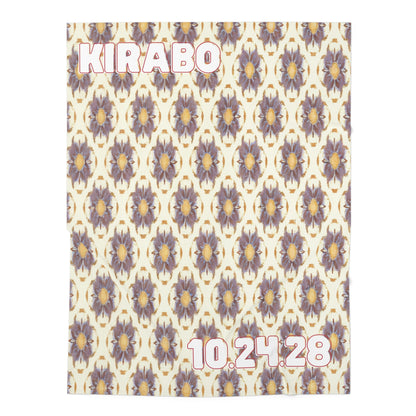 A cream personalized baby blanket with a repeating purple and gold floral pattern, inspired by African-inspired decor. KIRABO is in bold white and pink letters at the top left, with the date 10.24.28 in matching font at the bottom right.