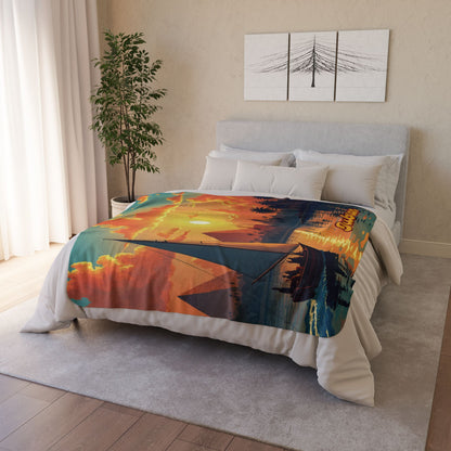 A neatly made bed with an African-inspired fleece blanket featuring a sunset, trees, and a lake scene. The room has light walls, a grey upholstered headboard, a potted plant in the corner, white curtains, and wall art above the bed for stylish home decor.