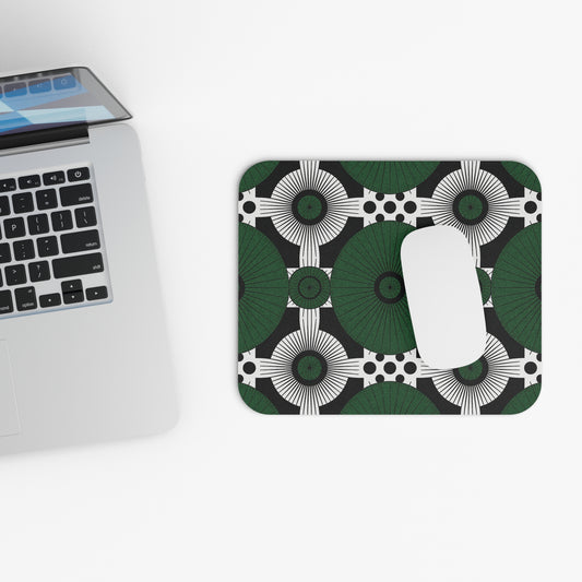 A silver laptop sits on a white surface next to an African-inspired mouse pad with a geometric pattern of green, black, and white circular shapes. A white wireless mouse rests on this non-slip desk accessory in a minimal and modern scene.