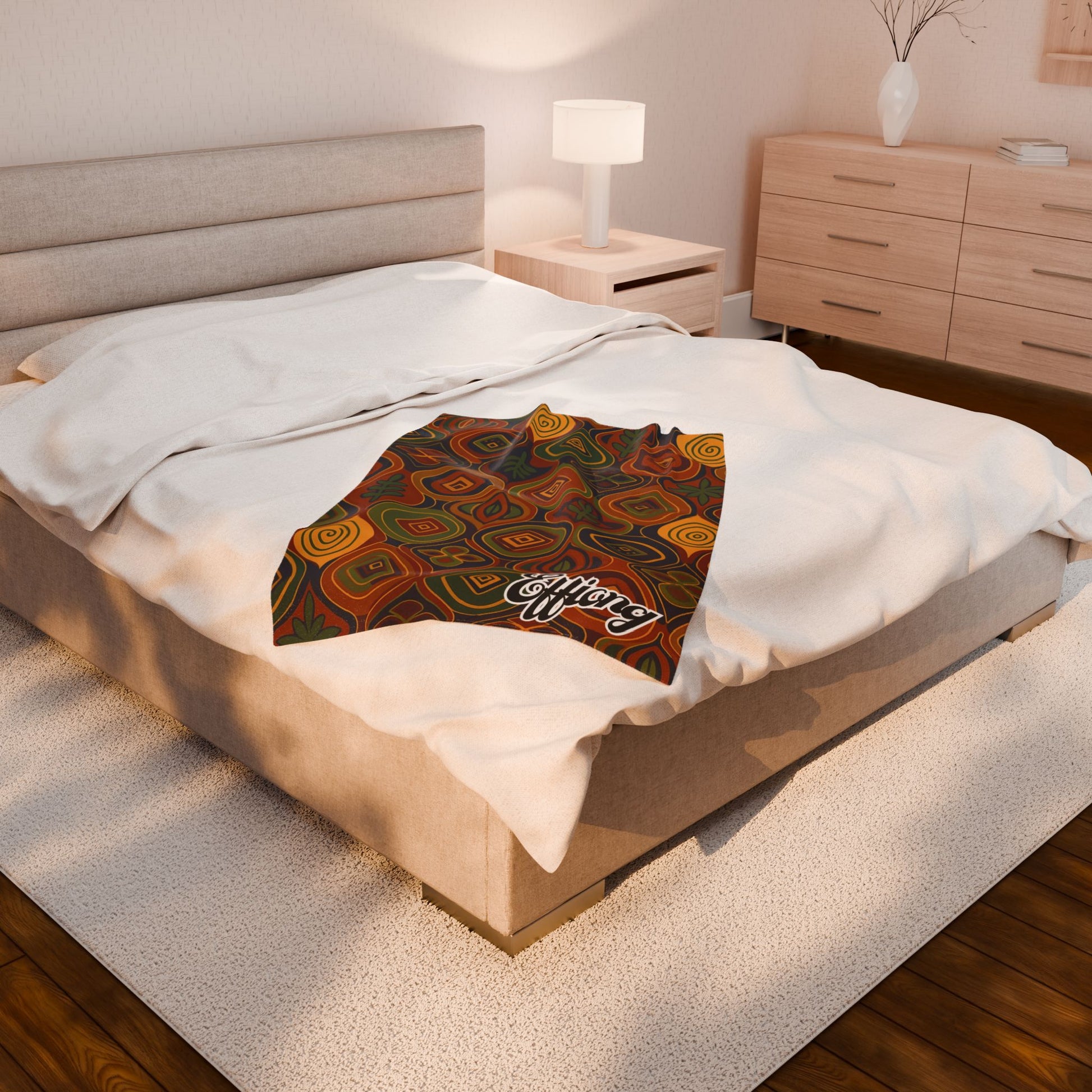 A modern bedroom features a beige upholstered bed with white bedding and an African-inspired blanket, patterned in the shape of Africa and labeled Africa. A wooden nightstand with a lamp and a dresser complete this cozy custom keepsake space.
