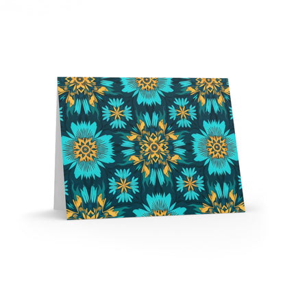 A folded card stands upright, featuring a vibrant floral pattern with large teal and blue flowers and smaller yellow-orange details on a dark background. The geometric, symmetrical design evokes African-inspired greeting cards for a bold, eye-catching appearance.