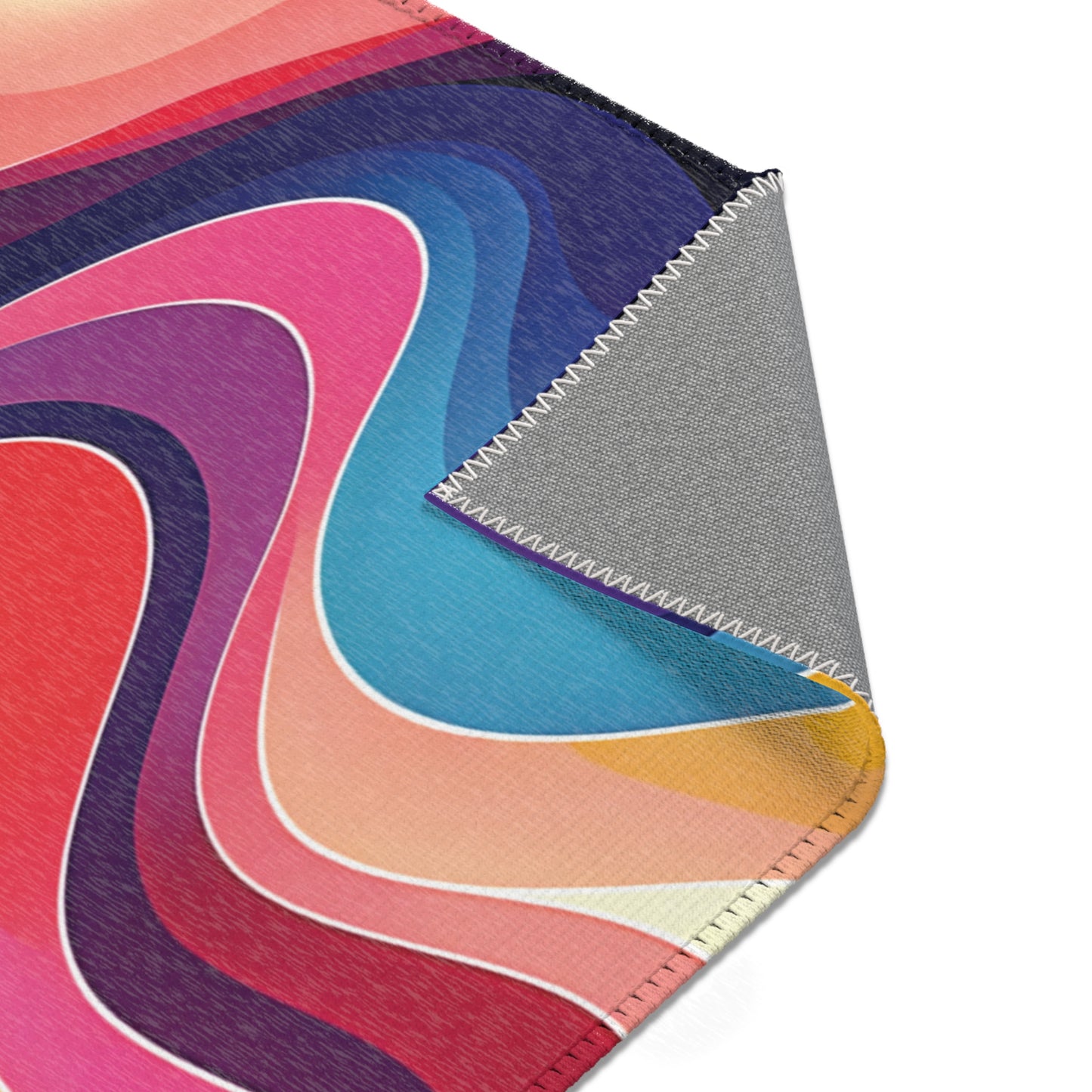 A colorful African-inspired abstract fabric with swirling, layered curves in pink, red, blue, purple, orange, and cream tones. The fabric’s corner is folded over, revealing a gray underside and white zigzag stitching along the edge.