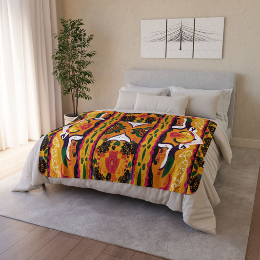 A neatly made bed with a vibrant, African-inspired fleece blanket featuring abstract patterns and stylized birds. The cozy home decor includes a light gray headboard, white bedding, a leafy plant, and minimalist wall art against cream-colored walls.