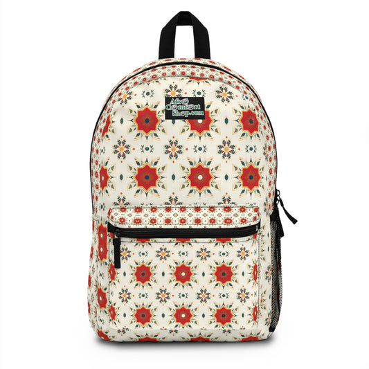 A white African-inspired backpack featuring a repeating pattern of red and orange star-shaped floral designs, with small blue and gold accents. It has a front zippered pocket, side mesh pocket, black top handle, and a black patch label on the front.