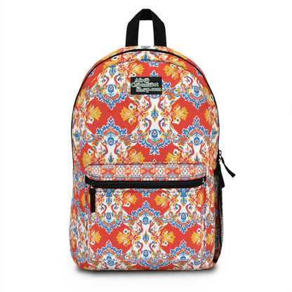 A colorful African-inspired backpack with intricate, vibrant red, blue, yellow, and white patterns. It features a front zippered pocket, black zipper pulls, a mesh side pocket, and a small patch on top with white and green text.