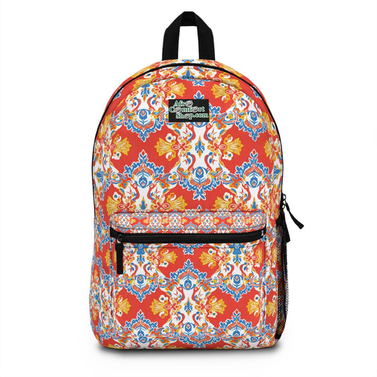 A colorful African-inspired backpack with intricate, vibrant red, blue, yellow, and white patterns. It features a front zippered pocket, black zipper pulls, a mesh side pocket, and a small patch on top with white and green text.