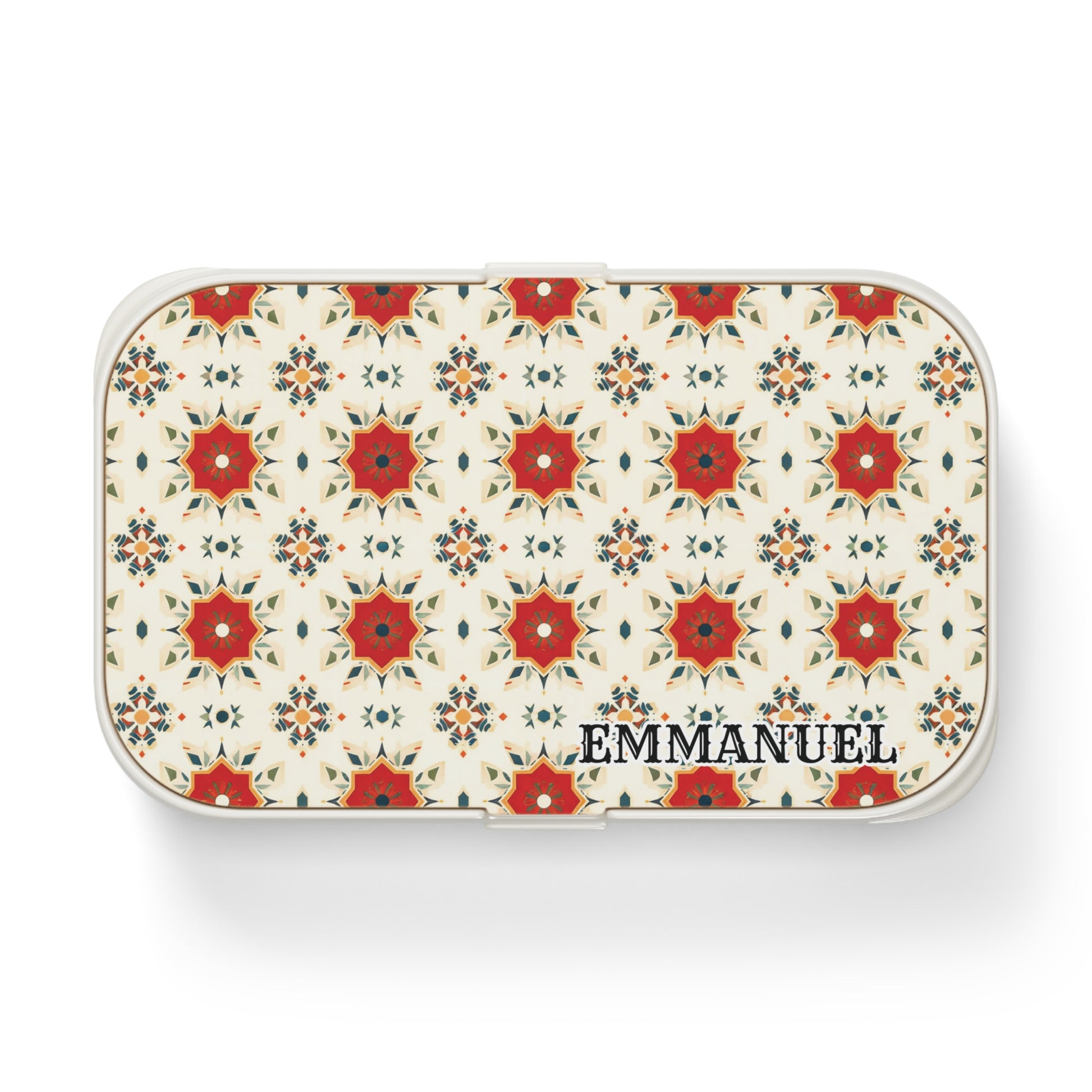 A rectangular white personalized lunch box features a repeating red and orange floral geometric pattern on the lid, inspired by African designs. EMMANUEL is printed in bold black letters in the lower right corner. The background is light cream.