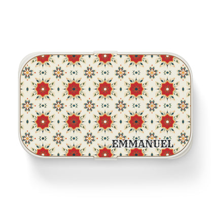 A rectangular white personalized lunch box features a repeating red and orange floral geometric pattern on the lid, inspired by African designs. EMMANUEL is printed in bold black letters in the lower right corner. The background is light cream.