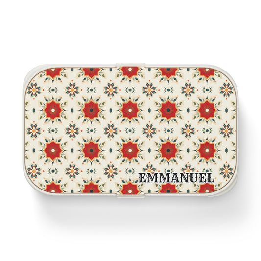 A rectangular white personalized lunch box features a repeating red and orange floral geometric pattern on the lid, inspired by African designs. EMMANUEL is printed in bold black letters in the lower right corner. The background is light cream.
