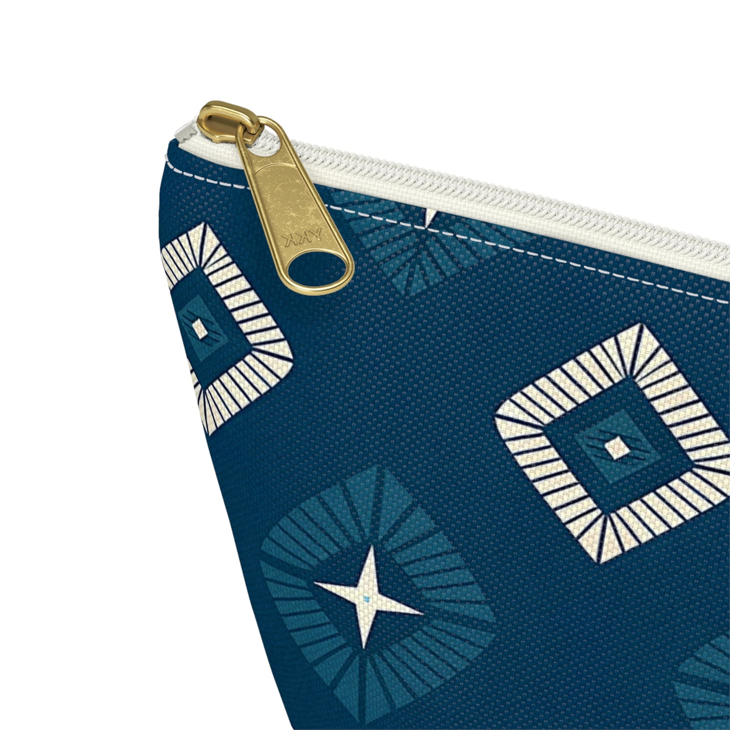 A close-up of a blue T-bottom pouch with a white zipper and gold pull. The pouch features African-inspired patterns with geometric squares and star shapes in white and dark blue. The textured fabric has visible stitching along the edge.