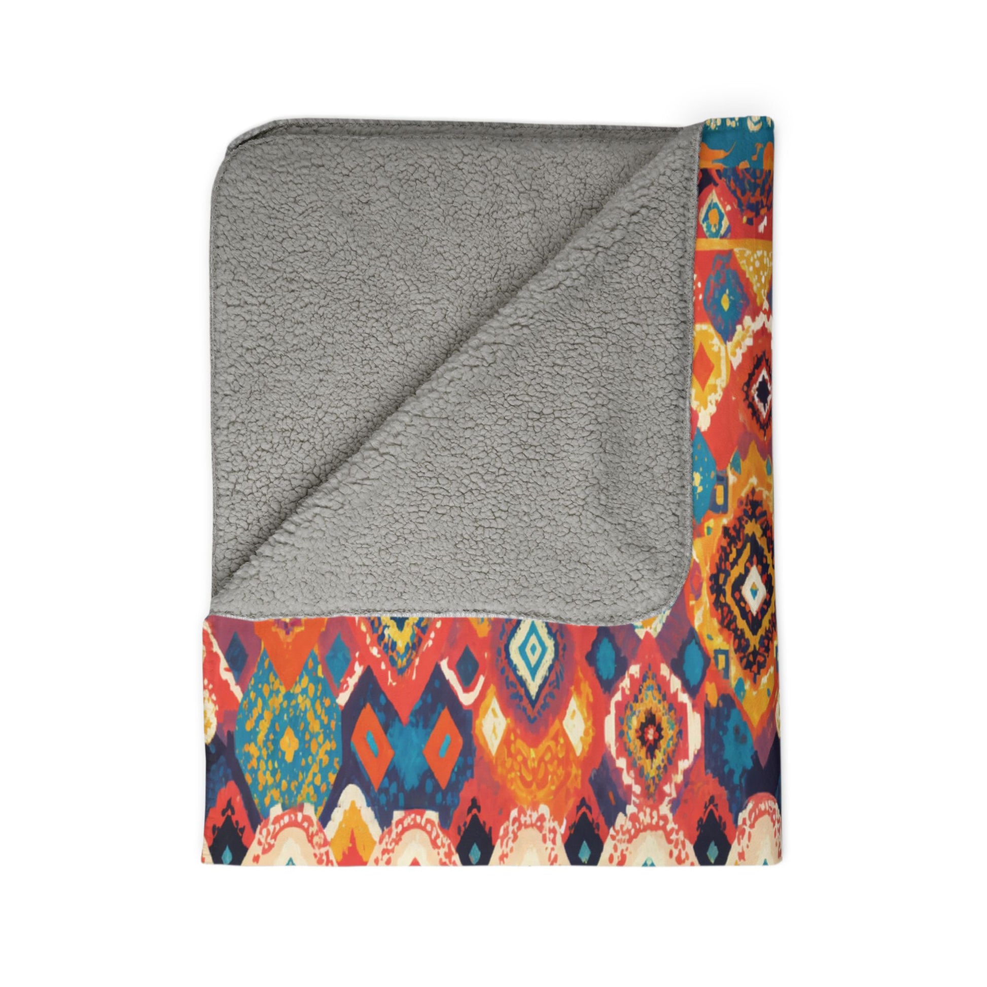 A square blanket with a gray, soft, fleece-like lining is shown folded so one corner reveals the underside. The top layer features an African-inspired colorful geometric pattern in red, yellow, orange, blue, and white tones.