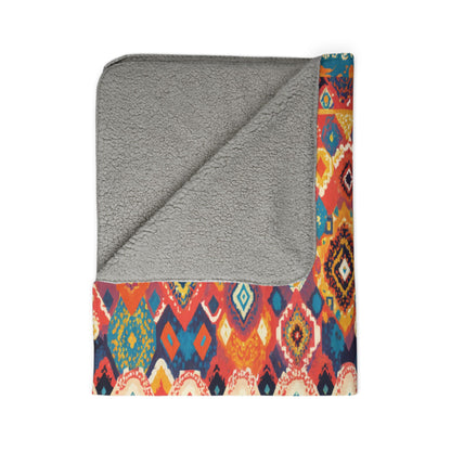 A square blanket with a gray, soft, fleece-like lining is shown folded so one corner reveals the underside. The top layer features an African-inspired colorful geometric pattern in red, yellow, orange, blue, and white tones.