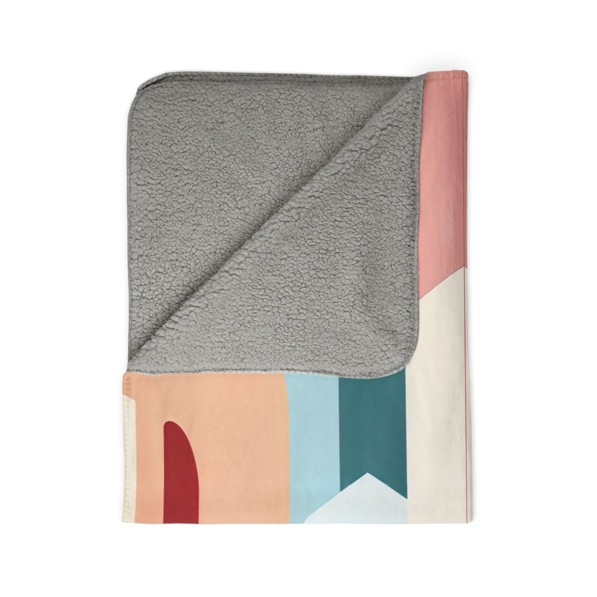 A folded blanket with a gray, soft, fleece-like lining and a colorful, African-inspired outer design featuring curved and geometric shapes in muted red, peach, blue, pink, and cream. The corner is turned over to show the contrasting textures.