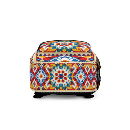 A colorful, square African-inspired backpack with black feet, featuring geometric and floral patterns in red, blue, yellow, and white. The bag has a black zipper on top and intricate, symmetrical designs on all visible sides.