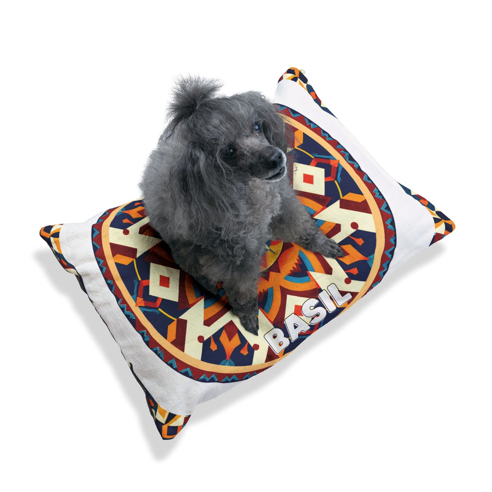 A small gray poodle sits on a personalized pet bed—a white pillow with a bold, colorful geometric pattern. “BASIL” is printed in white block letters on the durable construction, ensuring style and comfort against the plain white background.