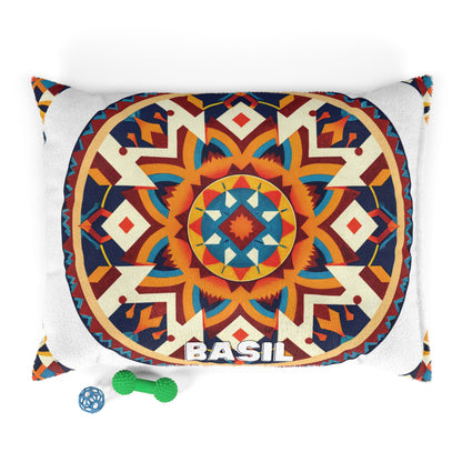 A rectangular pillow features a vibrant, symmetrical geometric mandala in red, orange, teal, yellow, and navy. “BASIL” is printed in bold white letters at the bottom. This personalized pet bed offers durable construction for lasting use. Two small dog toys—a blue ball and a green bone—are placed nearby on a white background.