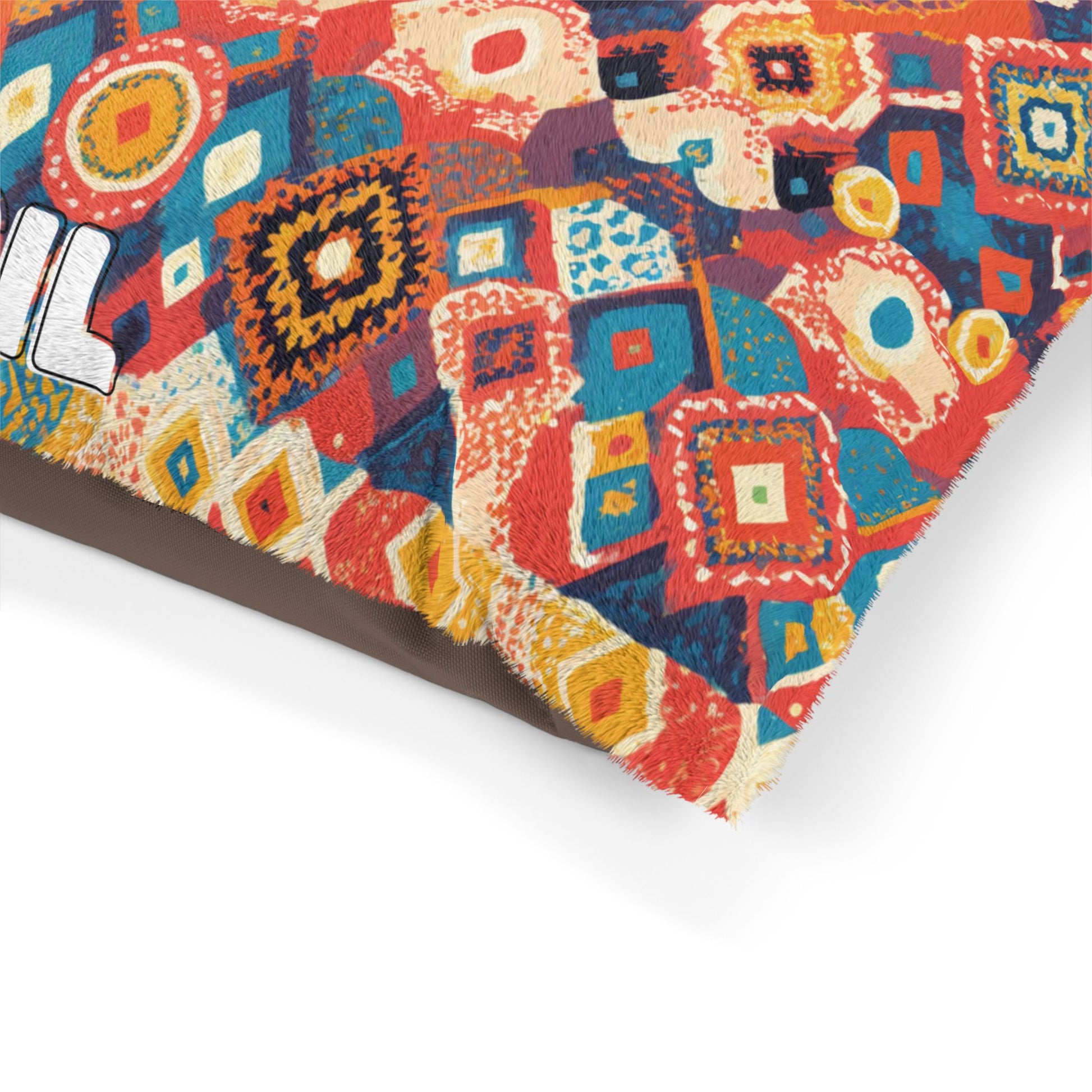 A close-up of a colorful cushion corner with a vibrant, African-inspired geometric patchwork pattern in red, orange, blue, and yellow hues. The fabric has a slightly frayed edge, and part of white, bold text is visible on the left side.