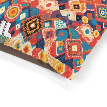 A close-up of a colorful cushion corner with a vibrant, African-inspired geometric patchwork pattern in red, orange, blue, and yellow hues. The fabric has a slightly frayed edge, and part of white, bold text is visible on the left side.