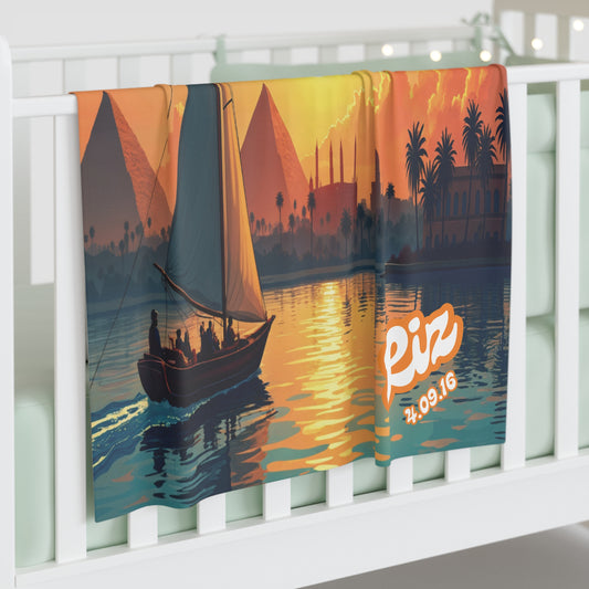A colorful personalized baby blanket draped over a white crib rail shows a sailboat with people on the Nile River at sunset, with the Pyramids of Giza and palm trees in the background. The word Eiz and the date 24.09.16 are printed in bold white and yellow text.