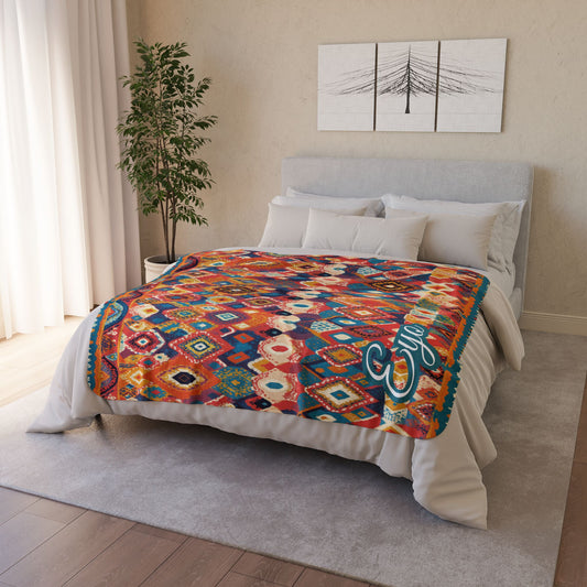 A neatly made bed with white bedding and an African-inspired geometric-patterned blanket in vibrant reds, blues, and yellows. The room features a gray headboard, white pillows, a green potted plant, and minimalist wall art above the bed.
