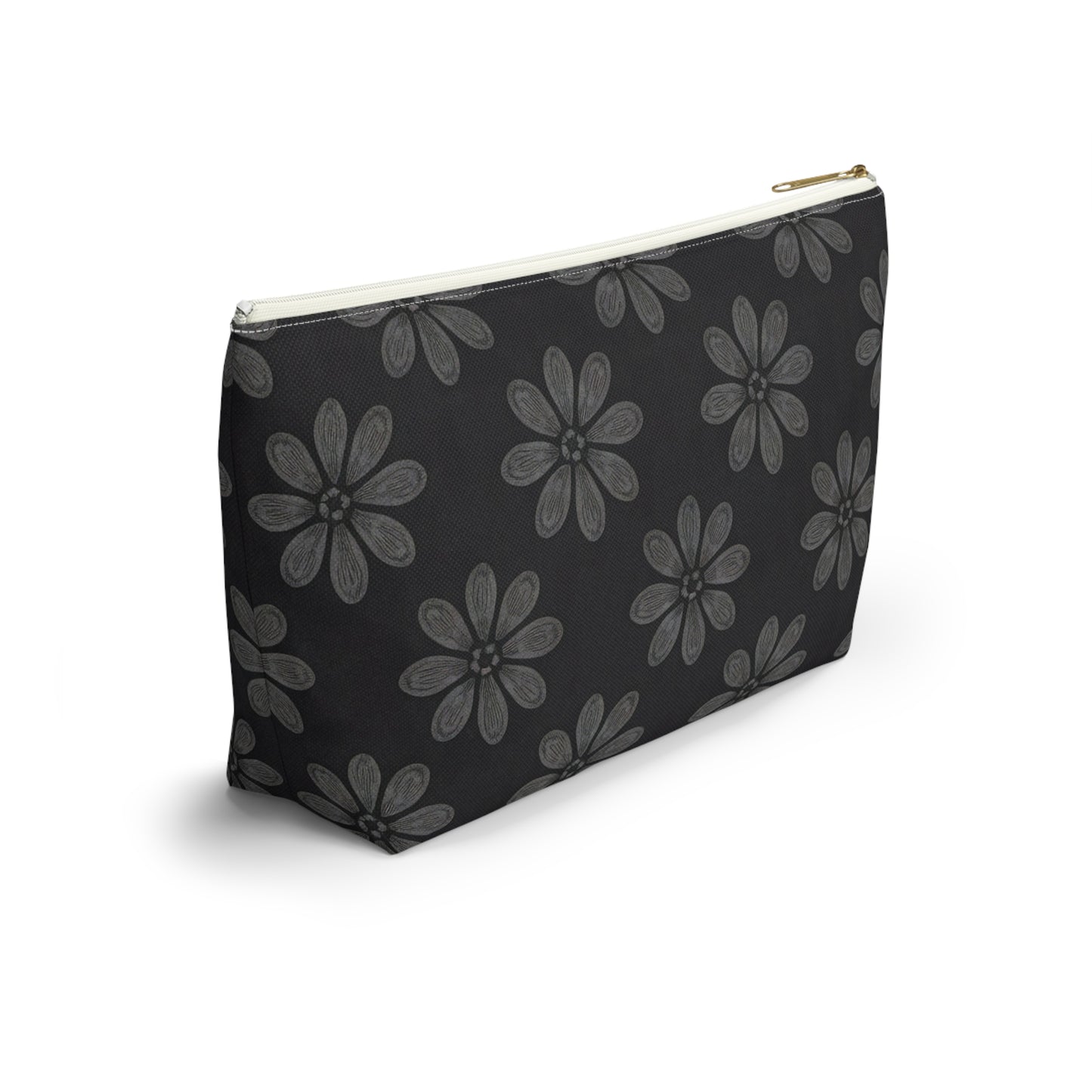 A black zippered cosmetic travel bag with a gold zipper is shown. The pouch features a repeating pattern of large, hand-drawn light gray daisies, inspired by African-inspired patterns, on a solid black background and rests on a white surface.