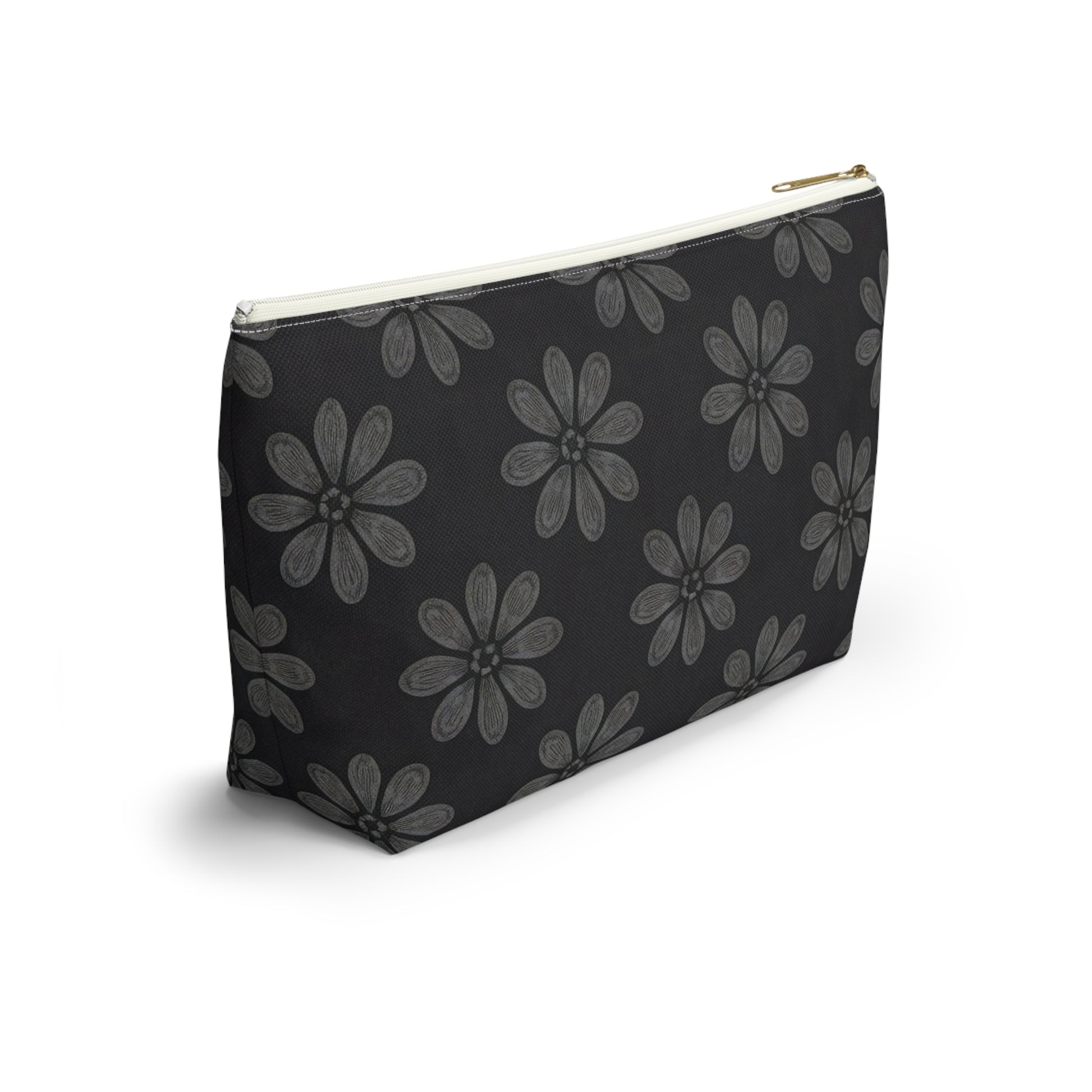 A black zippered cosmetic travel bag with a gold zipper is shown. The pouch features a repeating pattern of large, hand-drawn light gray daisies, inspired by African-inspired patterns, on a solid black background and rests on a white surface.