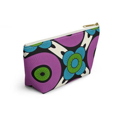 A T-bottom pouch with African-inspired patterns in bold, abstract florals of purple, green, blue, and black on white. Large circular flowers and organic shapes stand out, while a gold-colored zipper adds elegance—ideal as a cosmetic travel bag.