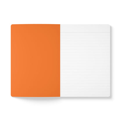 An open creative journal viewed from above; the left page is solid orange, while the right has light gray lines for daily journaling. The notebook rests on a white surface, maintaining a minimalistic and clean appearance.