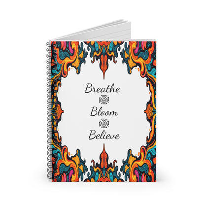 A spiral notebook with lined pages, featuring a white cover adorned by colorful, intricate paisley and African geometric patterns. The center showcases handwritten words: Breathe, Bloom, and Believe, stacked with decorative symbols between them.