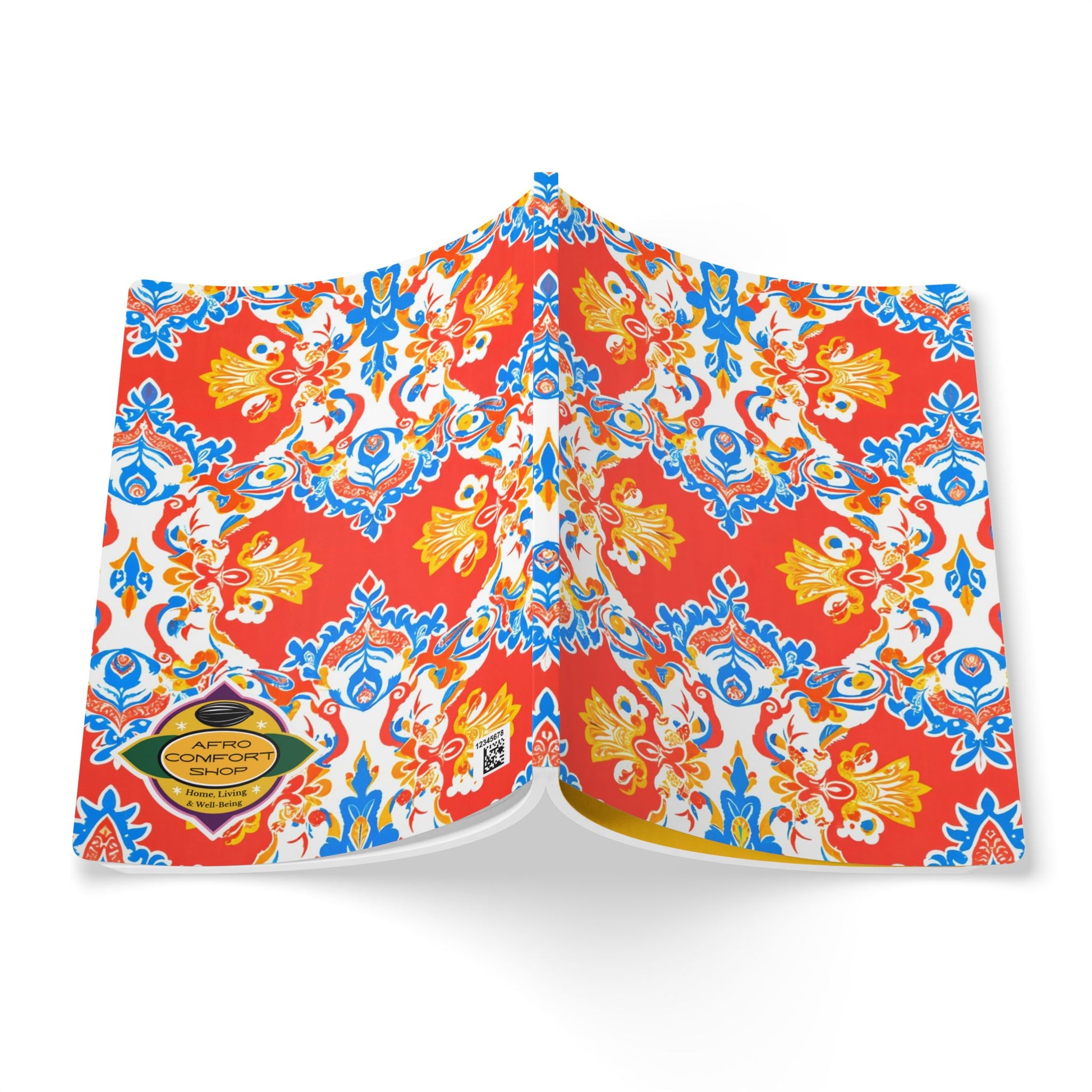 An open African-inspired journal with vibrant, symmetrical patterns in red, yellow, and blue on its cover and pages. A yellow and black label in the bottom left corner reads “Afro Comfort.” The book appears to be floating on a white background.