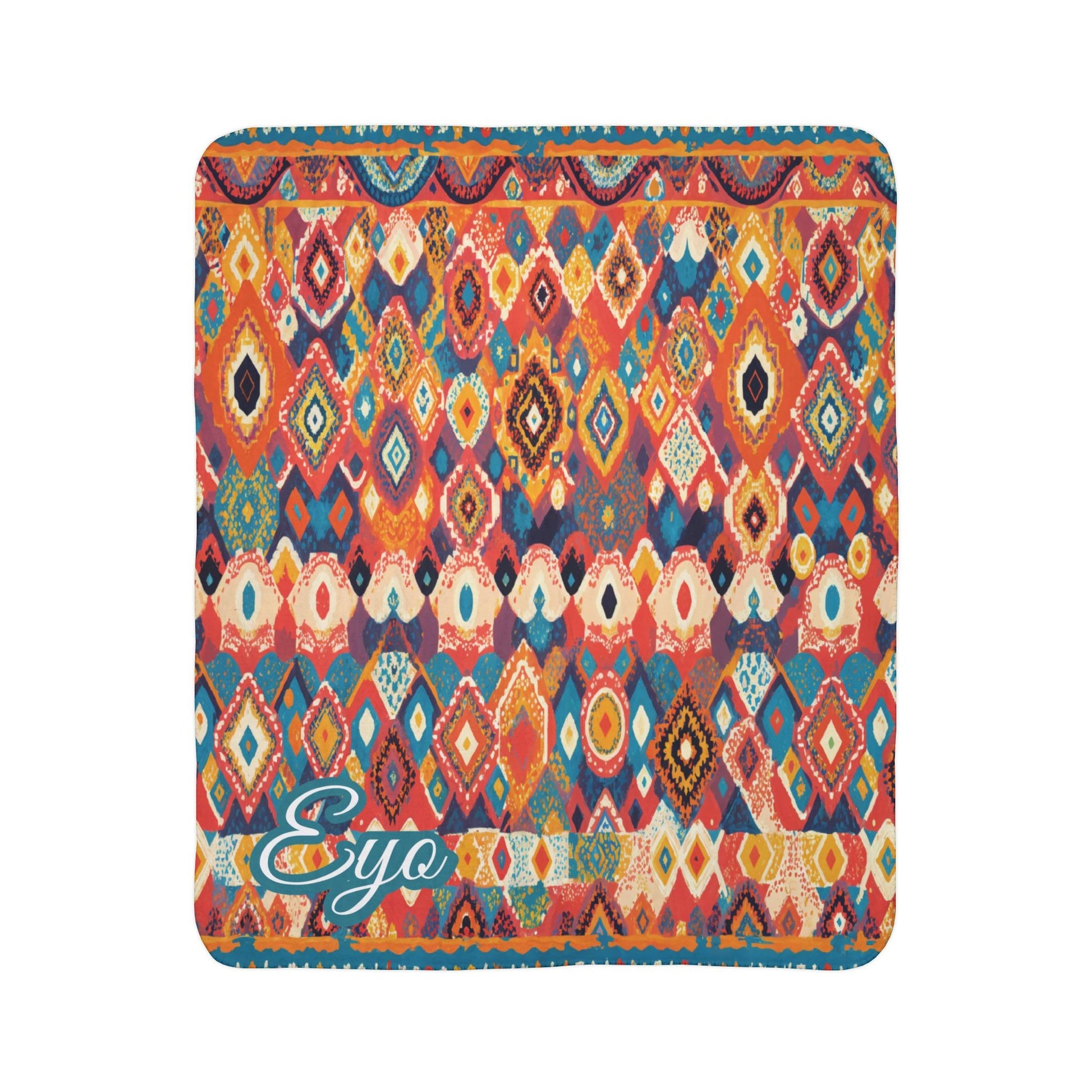 A colorful square blanket features a vibrant, African-inspired geometric pattern of diamonds, ovals, and zigzags in red, orange, blue, and yellow hues. The bottom-left corner displays the word Eyo in teal script with a white outline.