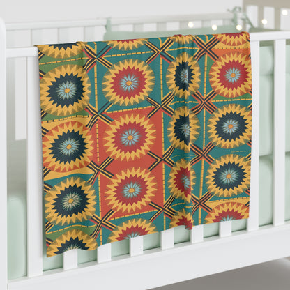 A colorful, customizable baby blanket with a bold geometric pattern in yellow, red, teal, and black—featuring concentric starbursts and squares—hangs over a white crib with mint green bedding. String lights glow softly in the background.