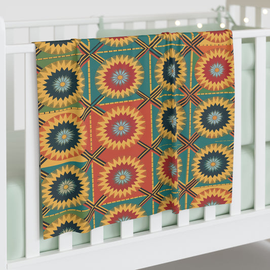 A colorful, customizable baby blanket with a bold geometric pattern in yellow, red, teal, and black—featuring concentric starbursts and squares—hangs over a white crib with mint green bedding. String lights glow softly in the background.