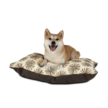 A Shiba Inu dog lies on an African-inspired beige and brown pillow bed with a happy expression, mouth open and tongue out. The bed features a starburst design on top and a solid brown base, set against a plain white background.
