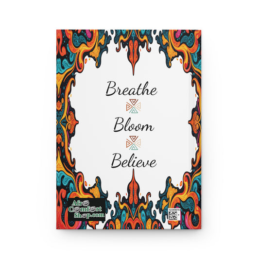 Colorful ornate border with swirling, abstract patterns frames a white center. In the middle, elegant black script reads: “Breathe Bloom Believe,” each word separated by a geometric design. Perfect as an African-inspired hardcover journal for wellness. Logo and QR code below.