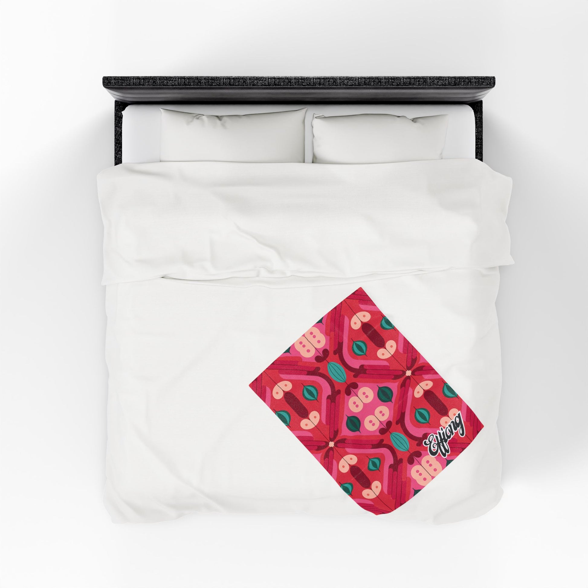 A white duvet cover on a bed features a vibrant, diamond-shaped red pattern inspired by African-inspired blanket designs, with abstract pink shapes, green leaves, and the word Enjoy in cursive at the bottom right corner.