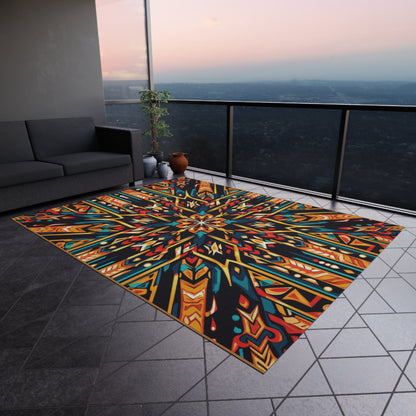A modern balcony with gray tile flooring features an African-inspired outdoor rug in colorful geometric patterns and weather-resistant polyester chenille. A gray sofa sits along the left wall, with potted plant and vases near the glass railing, overlooking a sunset cityscape.