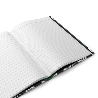 A close-up of an open hardcover journal with lined white pages. The cover has a black and white abstract pattern, and a green ribbon bookmark is visible in the center crease. The notebook rests on a white surface.