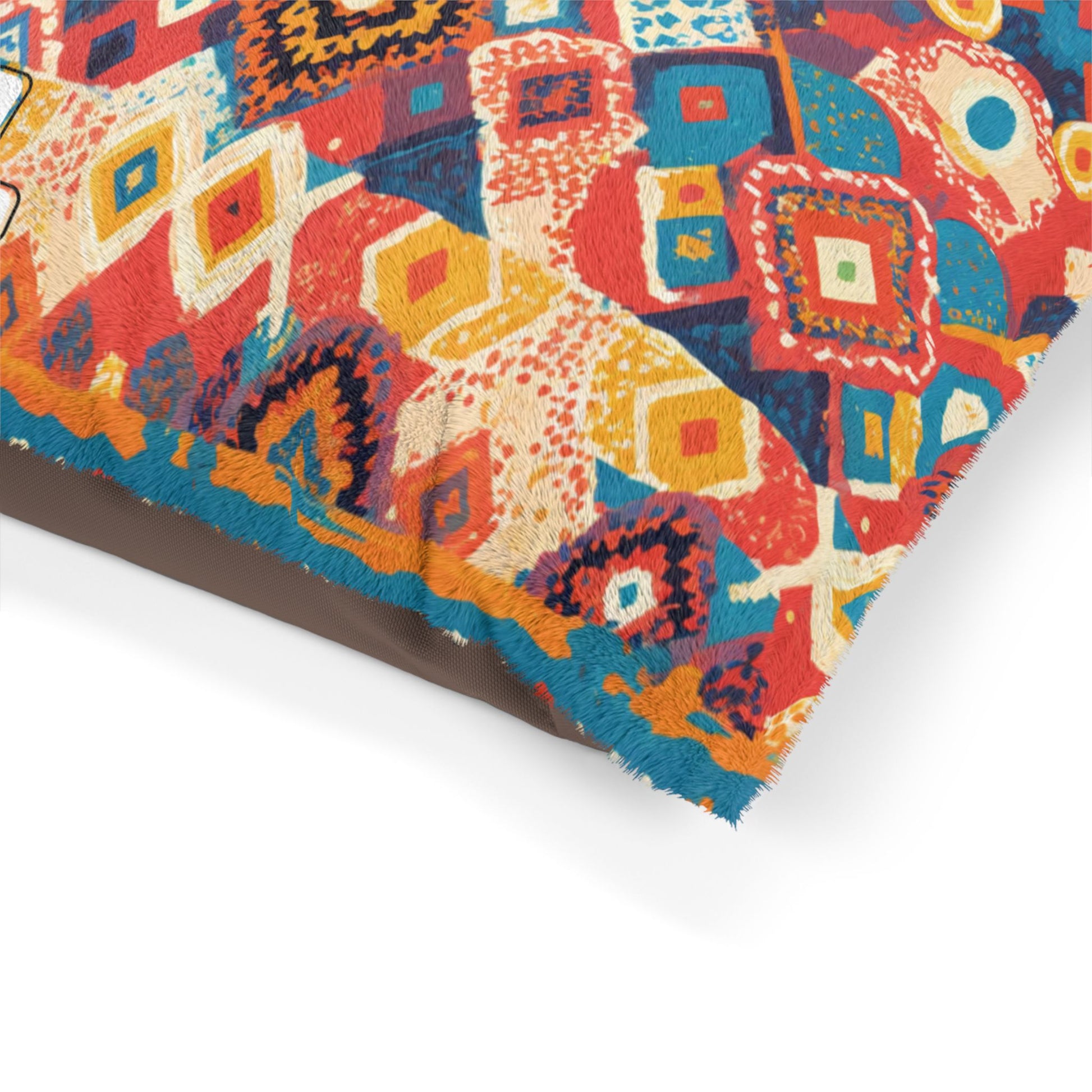 A close-up of a cushion corner with an African-inspired, bohemian-style geometric pattern in red, blue, yellow, cream, and orange tones. The textured fabric features a fringed edge, and the cushion rests on a plain surface.