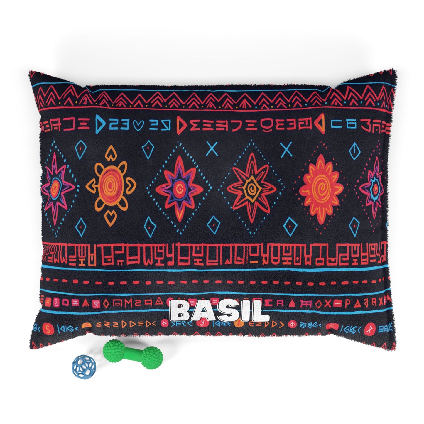 A black pillow with colorful tribal patterns in red, orange, pink, and blue features BASIL stitched in white. Below the pillow are two small dog toys: a green bone and a blue ball. Enjoy luxurious comfort with this personalized pet bed.