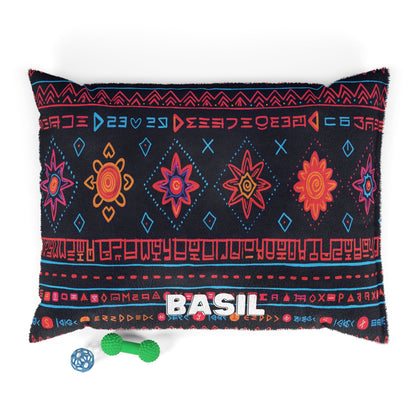 A black pillow with colorful tribal patterns in red, orange, pink, and blue features BASIL stitched in white. Below the pillow are two small dog toys: a green bone and a blue ball. Enjoy luxurious comfort with this personalized pet bed.