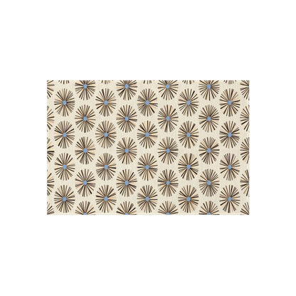 A beige rectangular surface features a repeating pattern of black starburst shapes with light blue centers, inspired by authentic African art designs. The geometric, mid-century modern look is enhanced by weather-resistant polyester chenille.