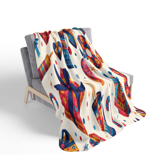 A gray chair draped with a festive sherpa fleece blanket decorated with colorful gift boxes, candy canes, ornaments, and bows in red, blue, yellow, and orange tones sits against a white background with small confetti-like dots.