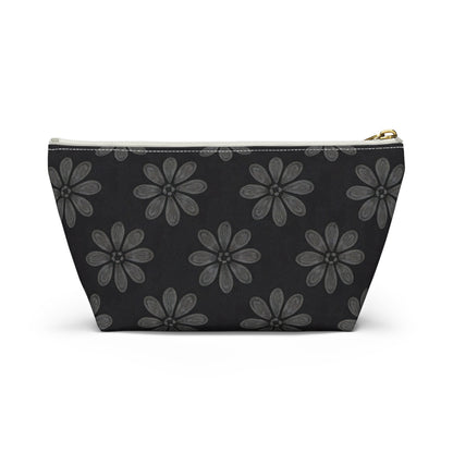 A zippered T-bottom pouch with a black background features a repeating pattern of large, stylized gray flowers with six petals each. The white zipper has a gold pull tab. Perfect as a cosmetic travel bag, it’s displayed against a plain white backdrop.