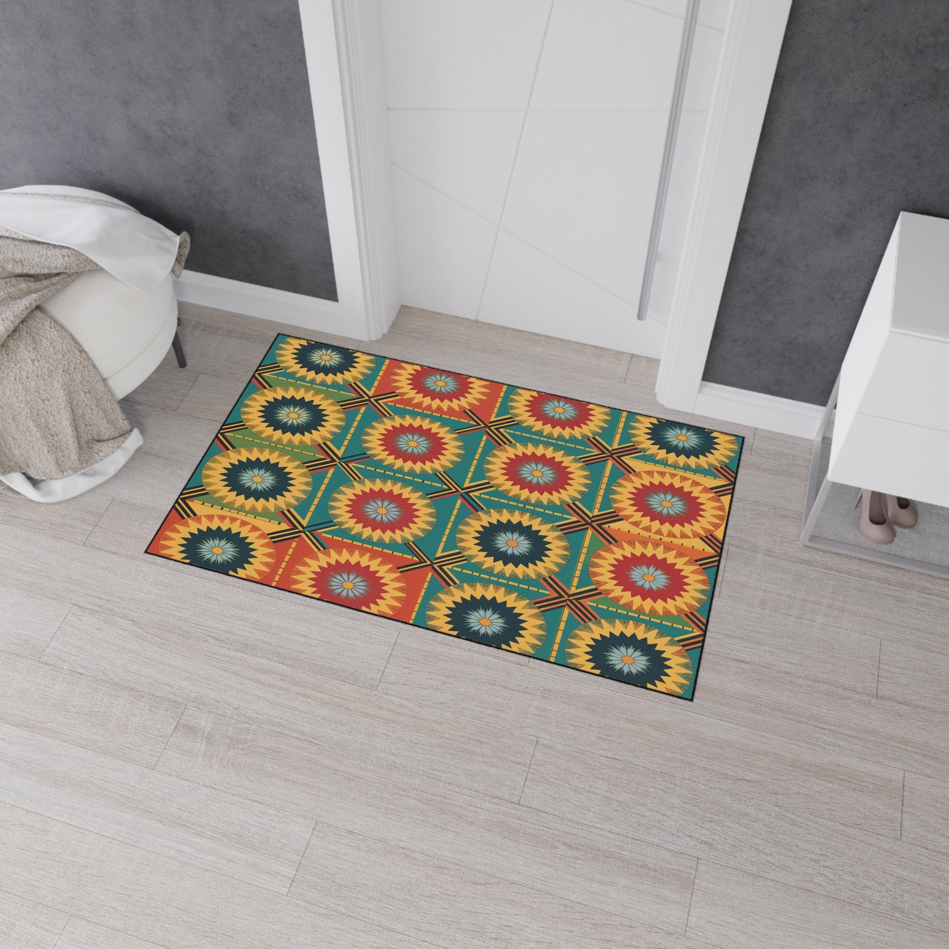 A colorful African-inspired floor mat with a geometric starburst pattern in red, yellow, green, and blue sits on light wooden flooring by a white doorway. It features non-slip rubber backing to keep it securely in place.