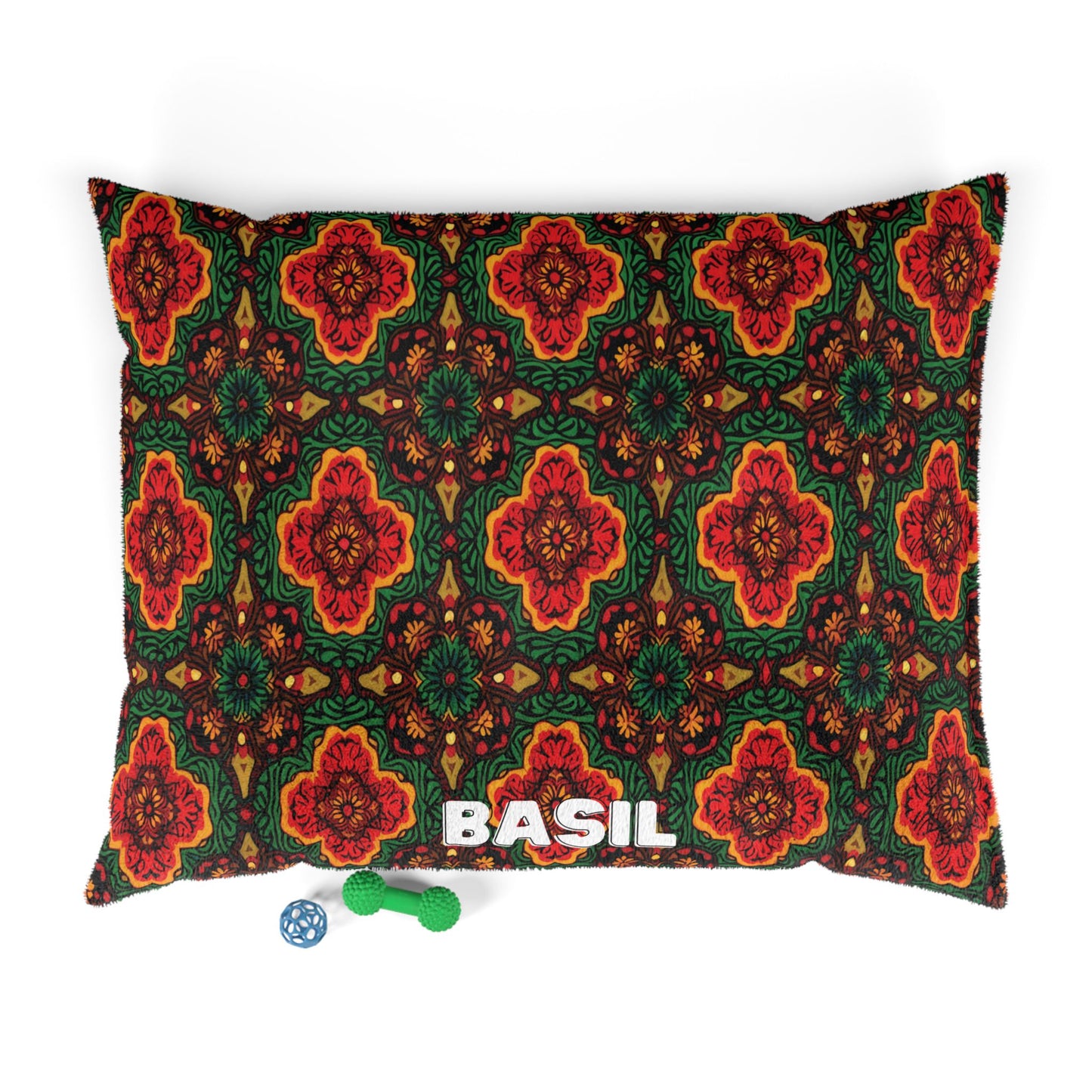 A rectangular pillow featuring a vibrant floral pattern in red, green, and black offers luxurious comfort. The name BASIL is printed in bold white letters at the bottom. Two dog toys—a blue ball and a green bone—rest nearby on a white background.