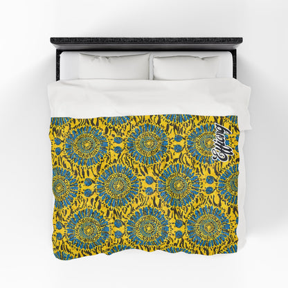 A bed with white pillows and an African-inspired blanket featuring bold yellow, blue, and black abstract circles; “Legacy” is written in stylish white script at the top right corner. The image is viewed from above.