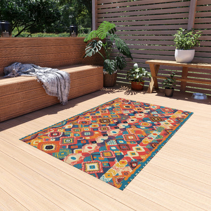 An African-inspired, colorful patterned rug with geometric and floral motifs lies on a light wooden patio. To the left, a wicker sofa with a gray throw sits among potted plants and a wooden bench. Sunlight filters through a slatted privacy screen.