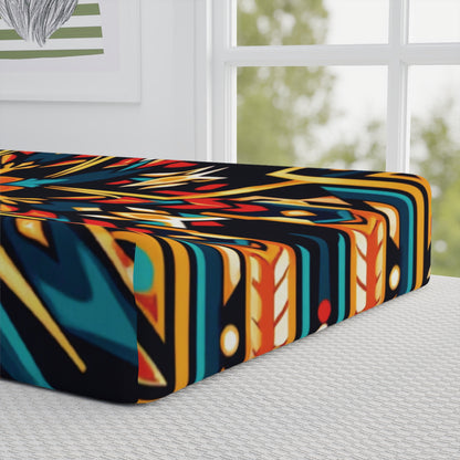 A close-up of a mattress with a bold, geometric, multicolored pattern reminiscent of an African-inspired nursery. The mattress rests on a light-colored textured base near a large window with greenery and framed wall art in view.