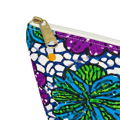 A close-up of a T-bottom pouch corner with a gold zipper pull. The fabric features African-inspired patterns in blue, purple, green, white, and yellow outlined in black, atop a textured canvas surface. Perfect as a cosmetic travel bag.